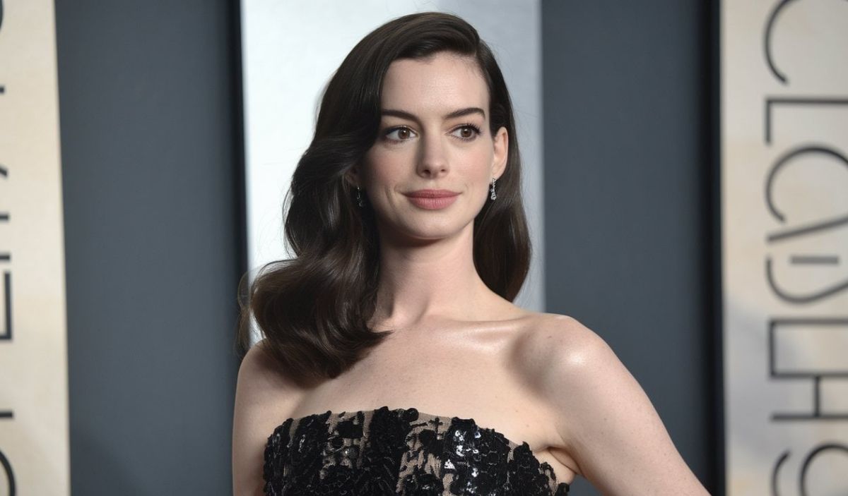 Anne Hathaway posing at an event, wearing a strapless black gown with her hair styled in soft waves.