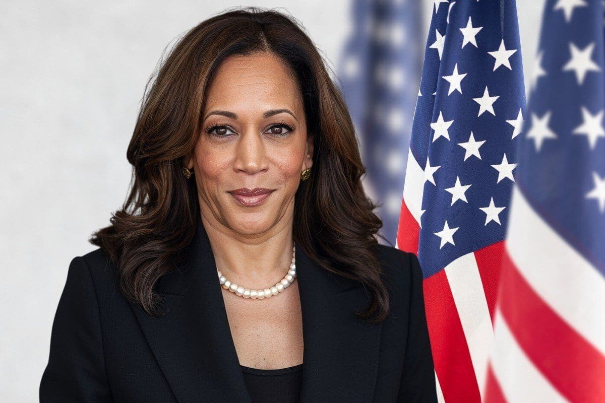 Kamala Harris standing in front of an American flag, wearing a black blazer and pearl necklace, with a calm and confident expression.