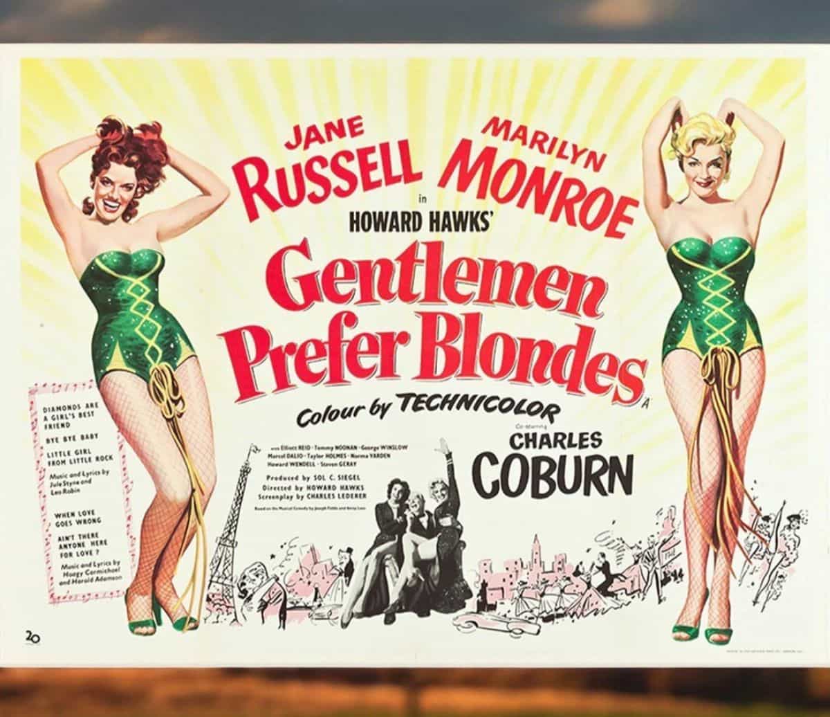 Vintage movie poster for Gentlemen Prefer Blondes, featuring illustrated versions of Marilyn Monroe and Jane Russell in green showgirl costumes with a background of cityscape drawings and colorful text.