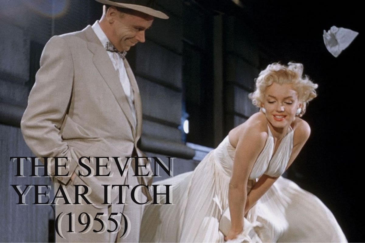 Tom Ewell in a light suit looks at a smiling woman in a white dress, holding it down as it blows upward, from the movie The Seven Year Itch (1955).